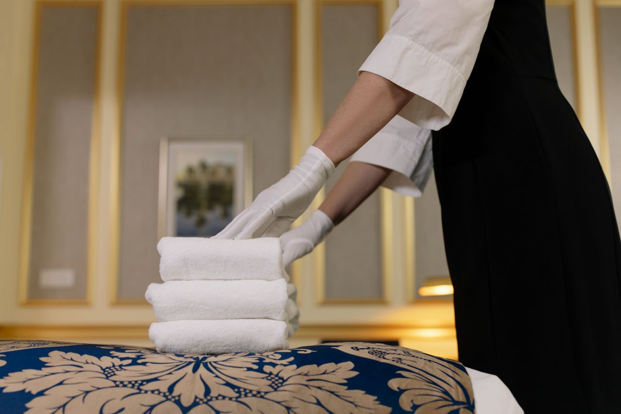 A hotel housekeeper neatly arranges fresh towels in a luxurious room setting.